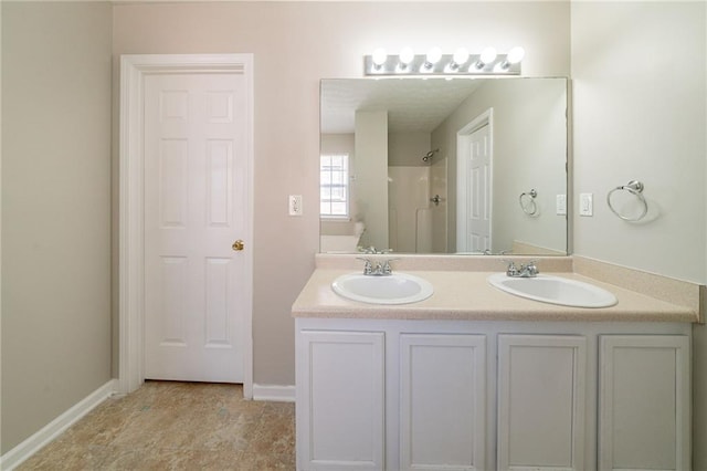 bathroom featuring double vanity, a sink, baseboards, and walk in shower