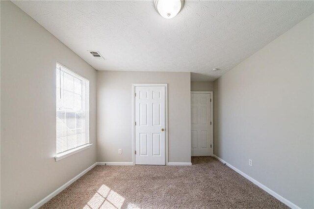 unfurnished bedroom with a textured ceiling, carpet flooring, visible vents, and baseboards