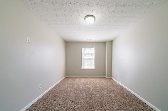 carpeted spare room featuring a textured ceiling and baseboards