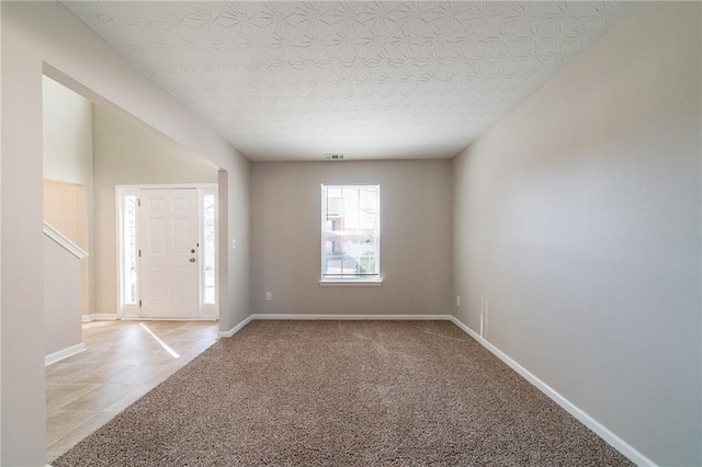 carpeted entryway with visible vents, a textured ceiling, and baseboards