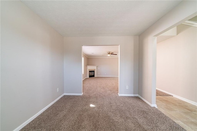 carpeted empty room featuring a textured ceiling, ceiling fan, a glass covered fireplace, and baseboards