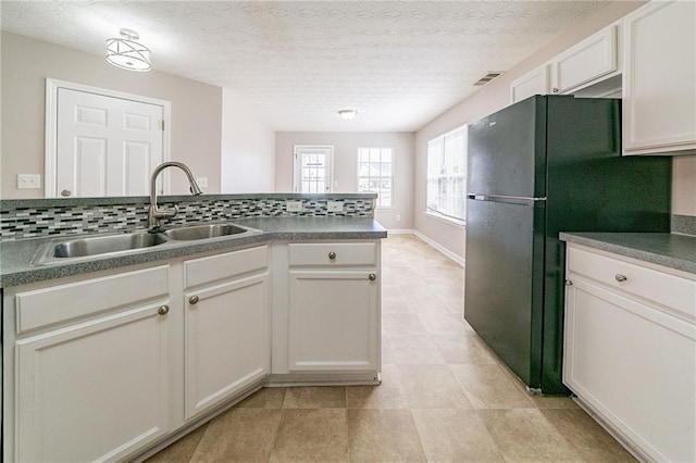 kitchen featuring tasteful backsplash, visible vents, a sink, and freestanding refrigerator