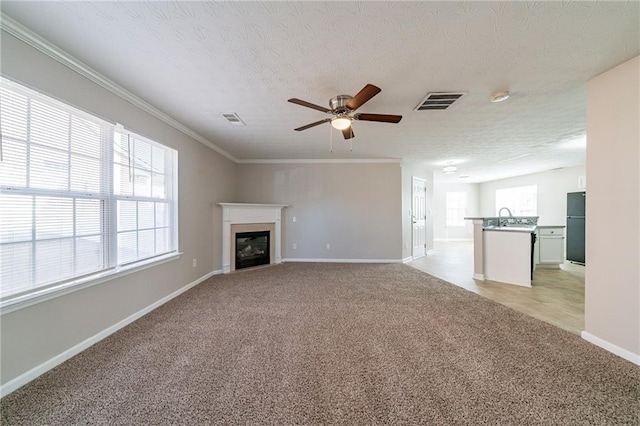 unfurnished living room featuring visible vents, a glass covered fireplace, crown molding, and light colored carpet