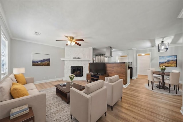 living room featuring crown molding, light hardwood / wood-style flooring, a fireplace, and ceiling fan