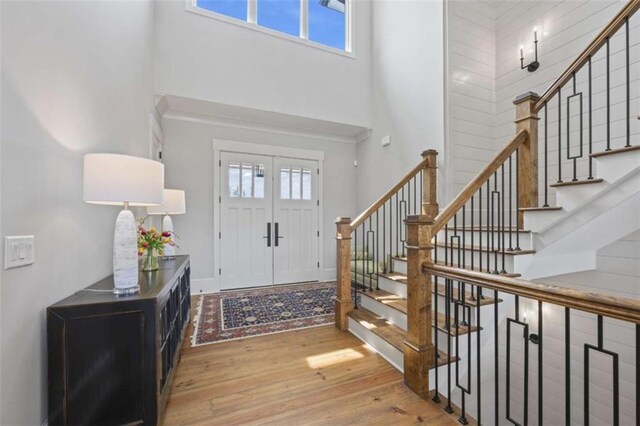 foyer featuring light wood-type flooring, french doors, a towering ceiling, and plenty of natural light