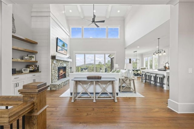 living room featuring sink, ceiling fan, light wood-type flooring, a fireplace, and beam ceiling