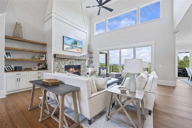 living room featuring ceiling fan, a fireplace, a towering ceiling, and hardwood / wood-style floors