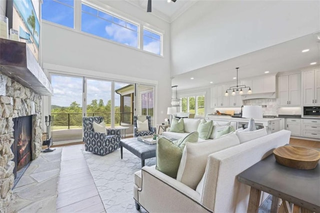 living room featuring a towering ceiling, a stone fireplace, ceiling fan, and ornamental molding