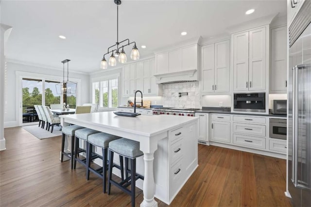 kitchen featuring decorative backsplash, decorative light fixtures, dark hardwood / wood-style floors, white cabinetry, and an island with sink