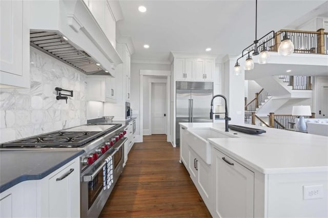 kitchen featuring backsplash, premium range hood, white cabinets, hanging light fixtures, and stainless steel appliances