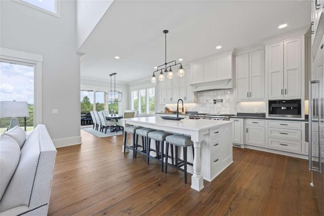 kitchen with built in microwave, white cabinetry, a center island with sink, and decorative light fixtures