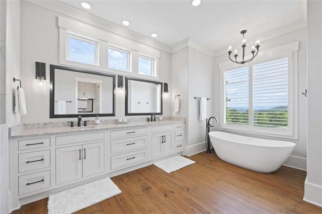 bathroom with a notable chandelier, vanity, wood-type flooring, and a tub to relax in