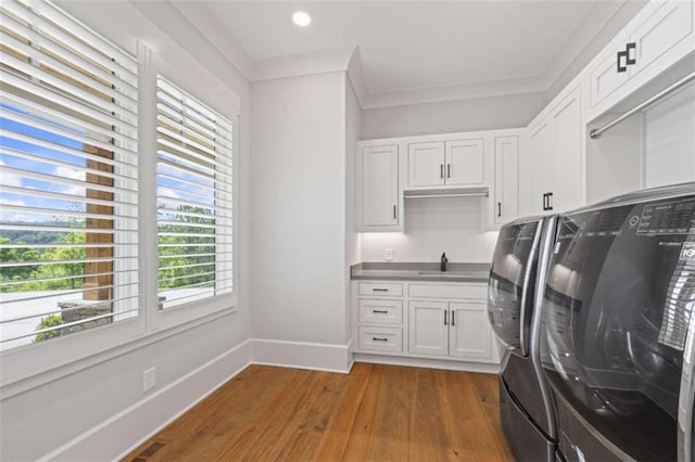 clothes washing area featuring washing machine and clothes dryer, sink, cabinets, dark hardwood / wood-style floors, and ornamental molding