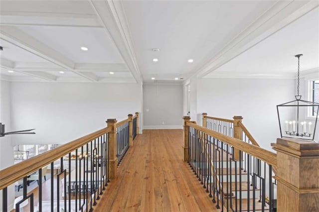 hallway featuring beam ceiling, coffered ceiling, ornamental molding, a chandelier, and light wood-type flooring