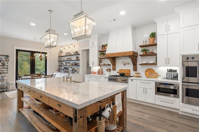 kitchen with white cabinets, pendant lighting, light stone counters, and custom range hood