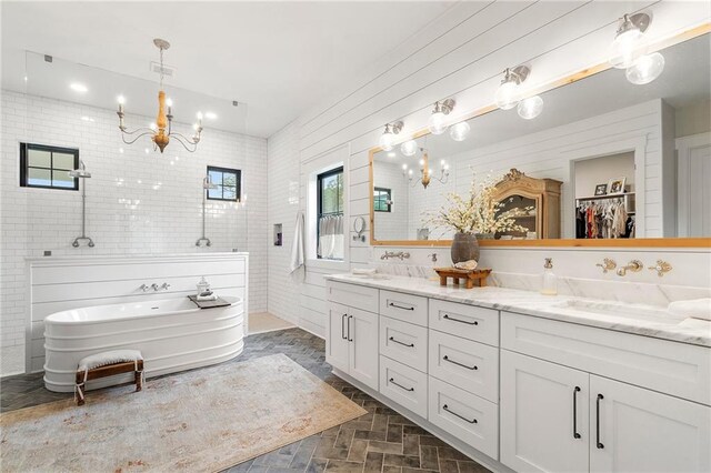 bathroom with vanity, independent shower and bath, tile walls, and a notable chandelier