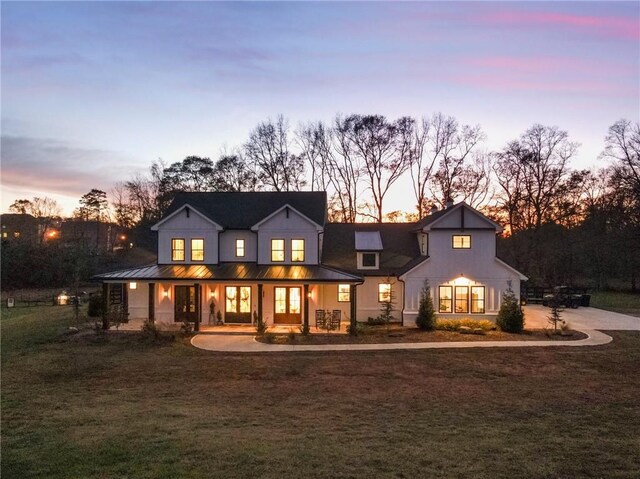 back house at dusk featuring a lawn and covered porch