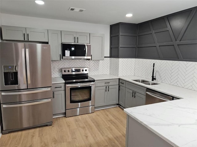 kitchen with gray cabinetry, sink, light hardwood / wood-style flooring, light stone counters, and stainless steel appliances