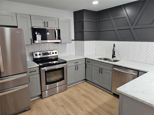 kitchen with light stone countertops, tasteful backsplash, stainless steel appliances, sink, and light hardwood / wood-style flooring