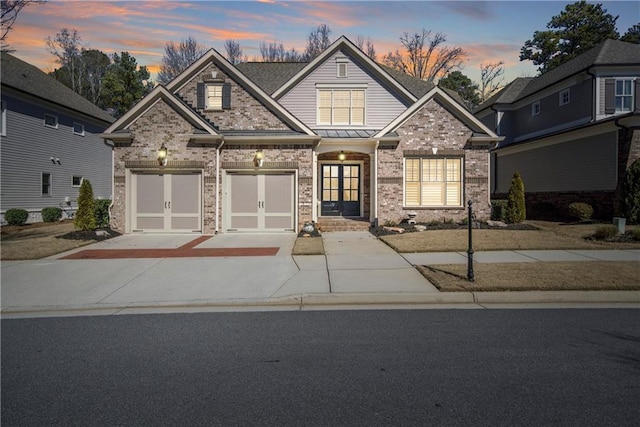 view of front of home featuring a garage, driveway, brick siding, and a standing seam roof