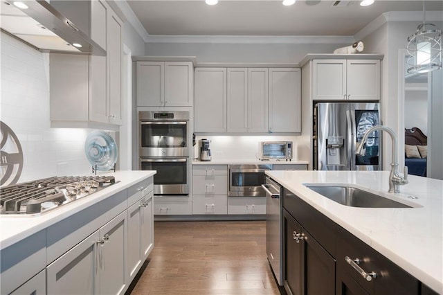 kitchen featuring stainless steel appliances, light countertops, ornamental molding, a sink, and wall chimney range hood