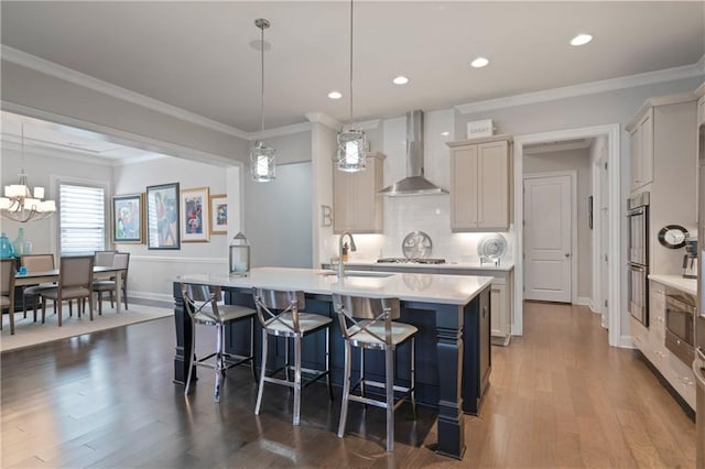 kitchen with wall chimney exhaust hood, a breakfast bar, a kitchen island with sink, light countertops, and a sink