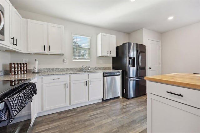 kitchen with white cabinets, sink, hardwood / wood-style flooring, appliances with stainless steel finishes, and light stone counters