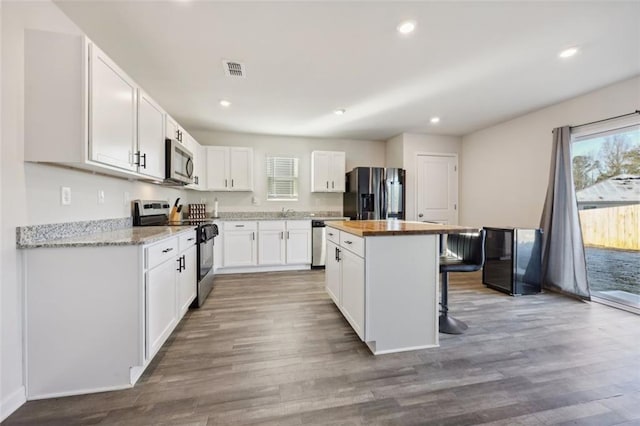 kitchen featuring white cabinetry, stainless steel appliances, a kitchen breakfast bar, wood-type flooring, and a kitchen island