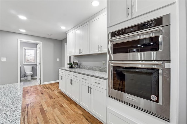 kitchen with light stone countertops, white cabinets, double oven, and light hardwood / wood-style floors