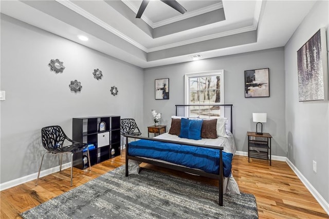 bedroom featuring hardwood / wood-style flooring, ceiling fan, ornamental molding, and a tray ceiling