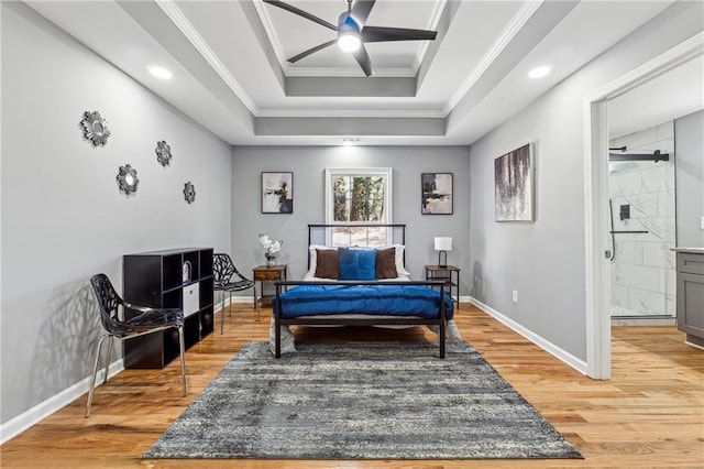 bedroom featuring crown molding, hardwood / wood-style flooring, ceiling fan, connected bathroom, and a tray ceiling