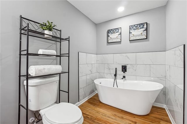 bathroom with tile walls, a tub to relax in, wood-type flooring, and toilet