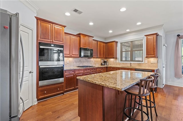 kitchen featuring visible vents, ornamental molding, a sink, wood finished floors, and stainless steel appliances