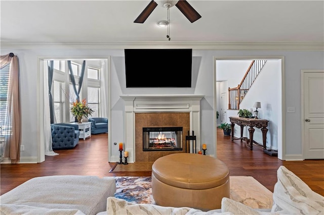 living area featuring wood finished floors, baseboards, stairs, a tiled fireplace, and crown molding