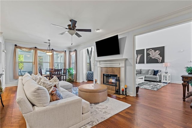 living area featuring crown molding, ceiling fan, baseboards, a tile fireplace, and dark wood-style flooring