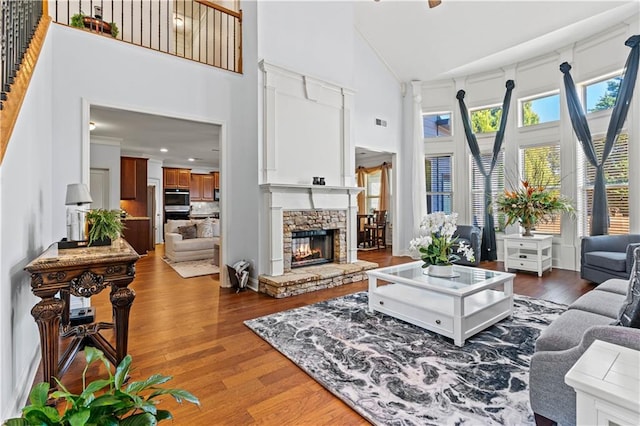 living area with wood finished floors, visible vents, high vaulted ceiling, a fireplace, and ornamental molding