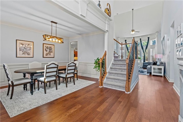 dining space with crown molding, stairs, wainscoting, wood finished floors, and a decorative wall