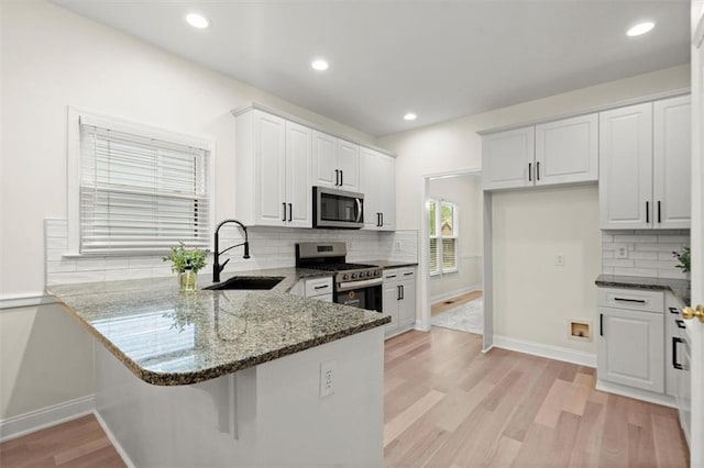kitchen featuring stainless steel appliances, a sink, dark stone countertops, light wood-style floors, and baseboards