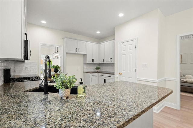 kitchen featuring a peninsula, dark stone counters, decorative backsplash, white cabinetry, and recessed lighting