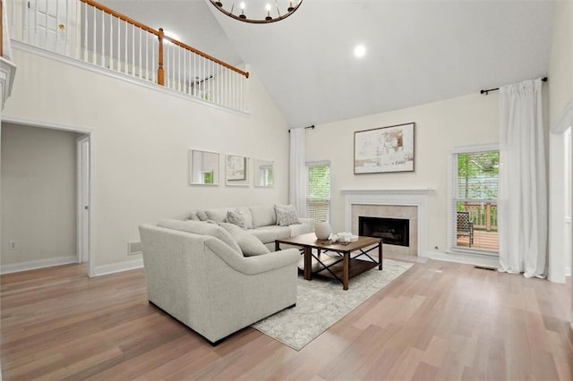 living room featuring high vaulted ceiling, light wood-style flooring, a fireplace, a chandelier, and baseboards