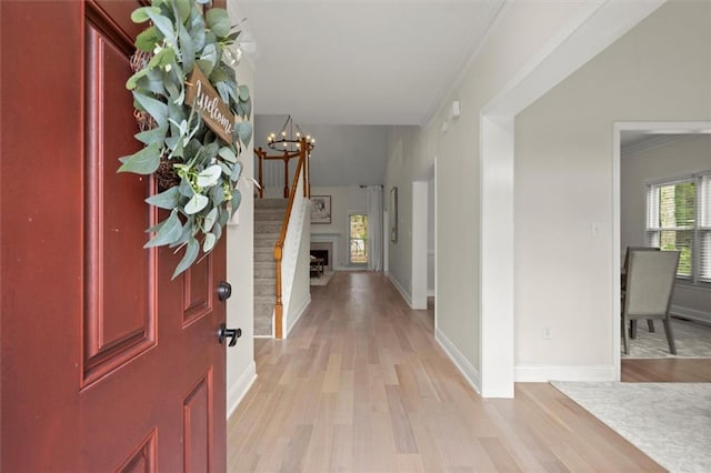 entrance foyer with light wood-type flooring, a chandelier, ornamental molding, baseboards, and a fireplace