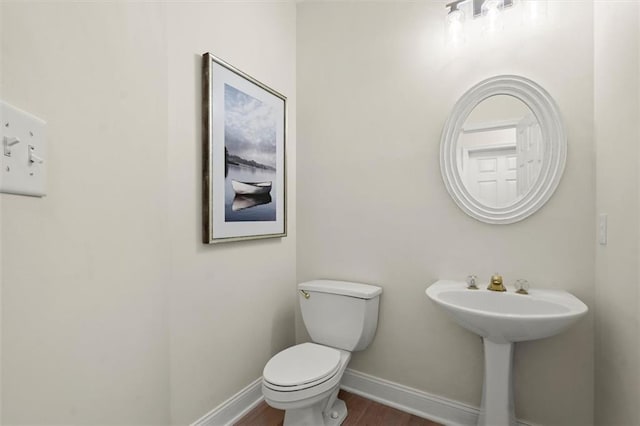 half bath with baseboards, wood finished floors, and toilet