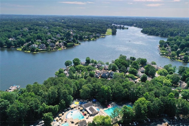 aerial view of property and surrounding area featuring a forest, a nearby body of water, and a pool