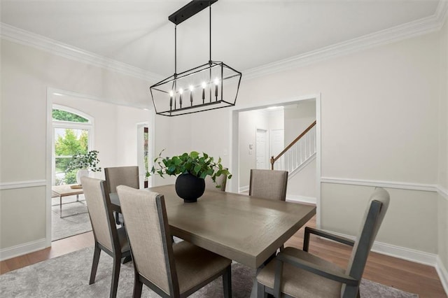 dining space featuring wood finished floors, ornamental molding, baseboards, stairs, and a chandelier