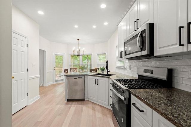 kitchen featuring stainless steel appliances, a sink, light wood-style flooring, tasteful backsplash, and a peninsula