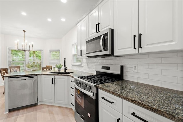 kitchen featuring appliances with stainless steel finishes, a sink, a chandelier, white cabinets, and a peninsula