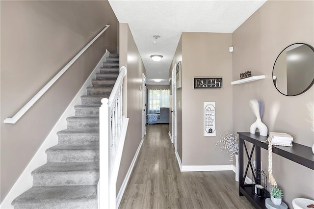 staircase with a textured ceiling, baseboards, and wood finished floors