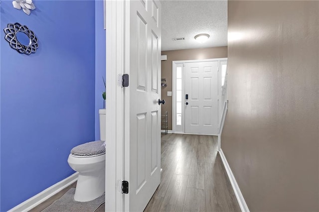 corridor featuring visible vents, wood finished floors, baseboards, and a textured ceiling