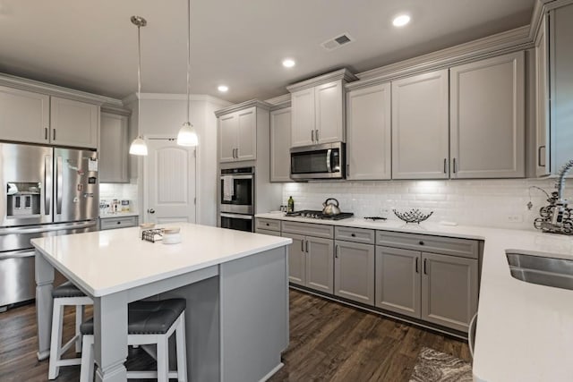 kitchen with gray cabinets, appliances with stainless steel finishes, dark hardwood / wood-style floors, decorative light fixtures, and a breakfast bar area