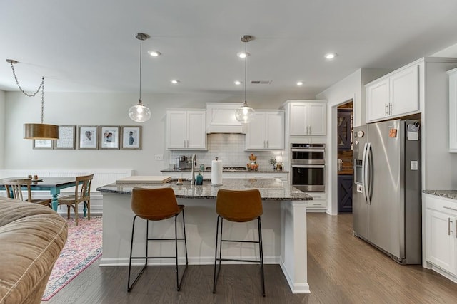 kitchen featuring white cabinets, stainless steel appliances, backsplash, and a kitchen bar